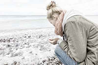 Woman collecting pebbles on shore against sky