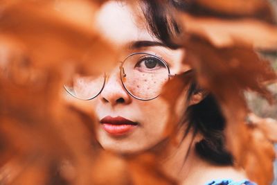 Close-up portrait of young woman seen through autumn leaves