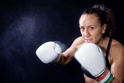 Portrait of woman practicing boxing against black background