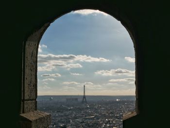 Distant view of eiffel tower seen through arch against cloudy sky