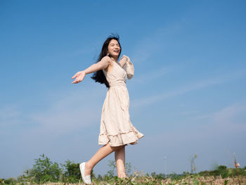 Full length of happy woman standing on field against sky