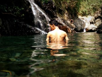 Rear view of shirtless man swimming in water