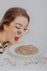 Close-up of woman wearing sunglasses with confetti against gray background