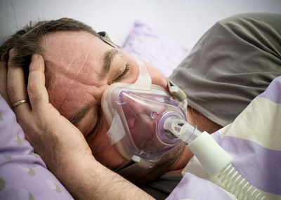 Close-up of patient wearing oxygen mask while lying on bed in hospital