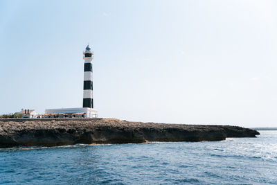 Lighthouse by sea against clear sky