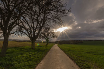 Empty road amidst grassy field against cloudy sky