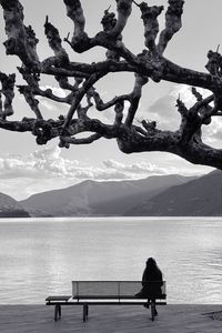 Rear view of woman sitting on bench by sea against sky