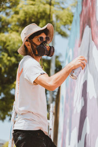 Person wearing gas mask spray painting on wall outdoors