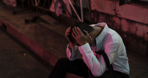 High angle view of man listening music while sitting on footpath at night