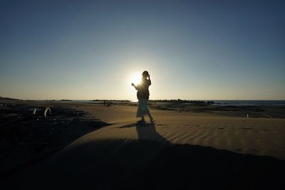 Silhouette woman standing at beach against clear blue sky