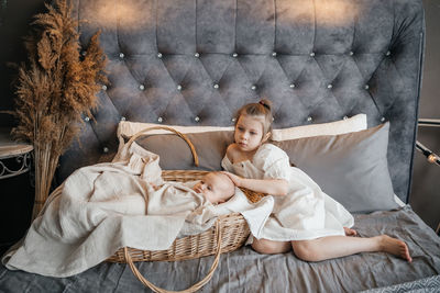 Girl taking care of her younger sister on the bed wicker basket hugs