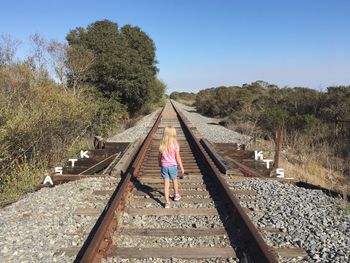 Rear view of girl walking on railroad track against clear blue sky
