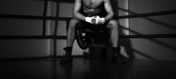 Low section of shirtless man sitting on chair in darkroom