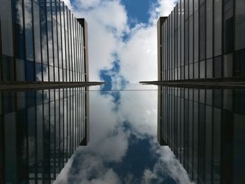 Directly below view of modern buildings reflection on glass window against sky