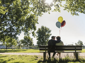 Happy senior couple with balloons sitting on bench in a park