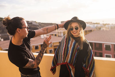 Man holding hat on happy girlfriend head at building terrace