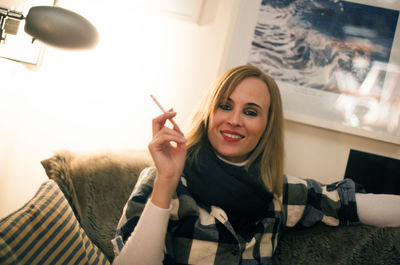 Portrait of beautiful woman holding cigarette while sitting on sofa
