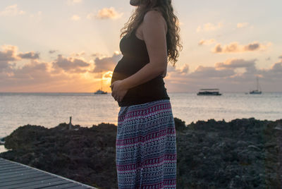 Woman standing at beach against sky during sunset