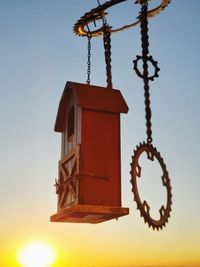 Low angle view of birdhouse hanging against sky during sunset