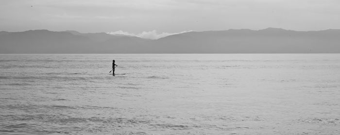 Silhouette man paddleboarding in river against mountains