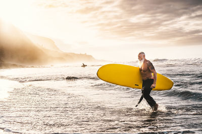 Man with surfboard on sea shore against sky