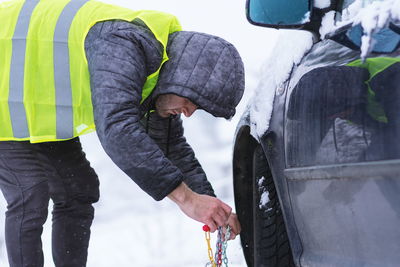 Man putting chain on tire of car during snow 