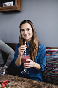 Portrait of smiling young customer having drink while sitting at dining table in restaurant