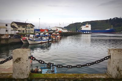 Boats moored at harbor by river against sky