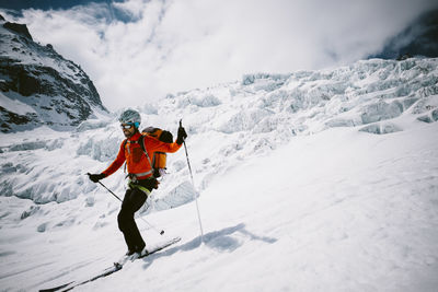 Man skiing on snow covered mountain against cloudy sky
