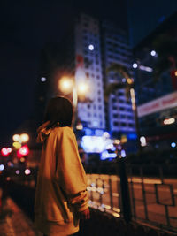 Rear view of woman standing on illuminated street at night