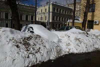 Snow covered street by buildings in city