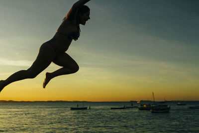 Silhouette man jumping in sea against sky during sunset