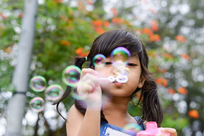 Low angle portrait of cute girl blowing bubbles at park