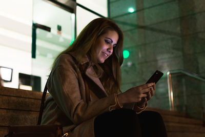 Young woman writes a message in her smartphone on the street at night