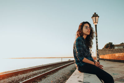 Portrait of woman sitting on railroad track against clear sky