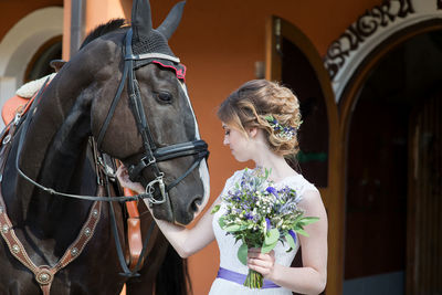 Beautiful bride holding flower bouquet by brown horse