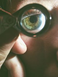 Close-up portrait of person holding magnifying glass on eye