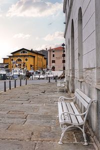 Empty chairs on street by buildings against sky