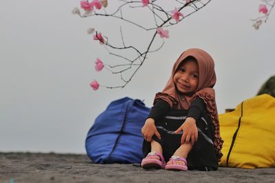 Portrait of smiling girl wearing hijab sitting on land against clear sky