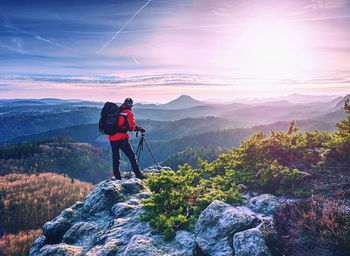 Photographer with tripod hold tripod, stand on rock. hiker admiring stunning misty mountain range