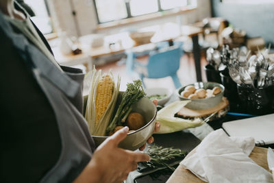 Midsection of female chef holding bowl of vegetables in studio kitchen