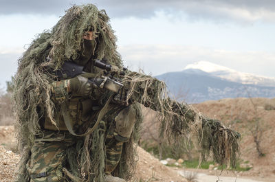 Sniper holding rifle against sky