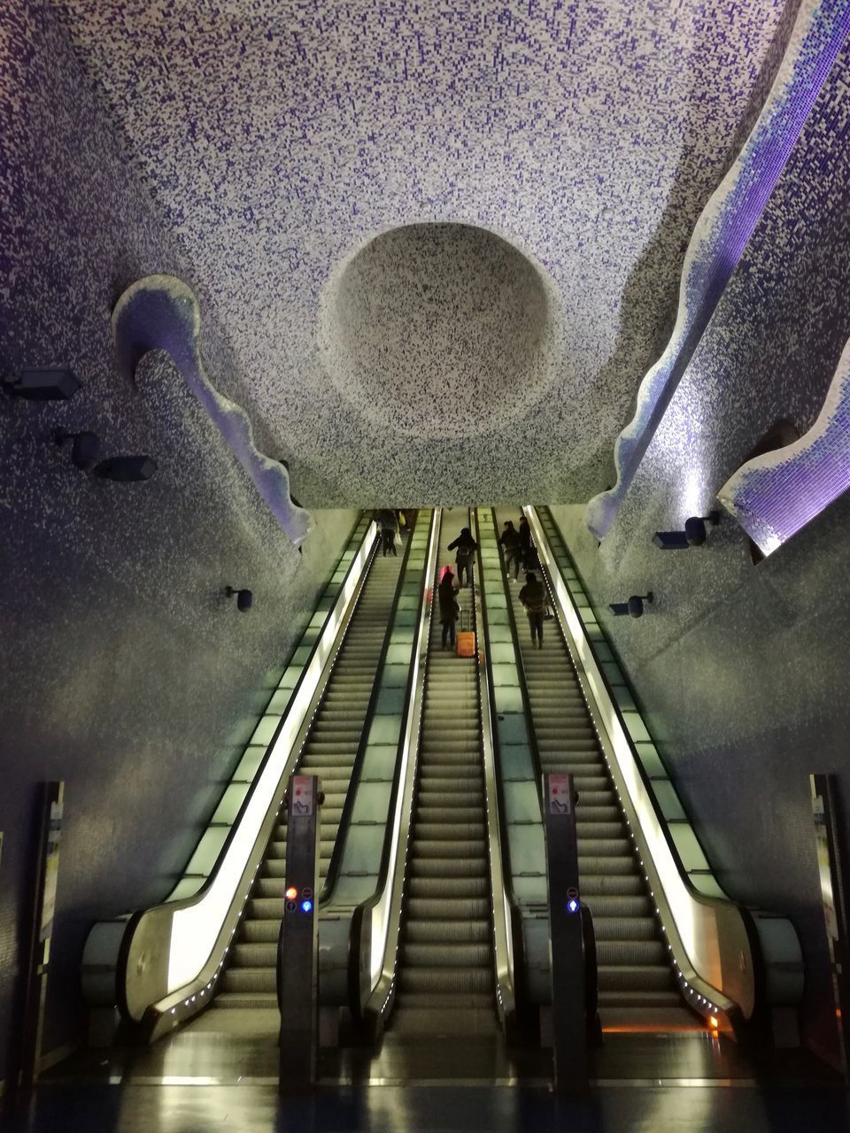 PEOPLE ON STAIRCASE IN ILLUMINATED UNDERGROUND WALKWAY