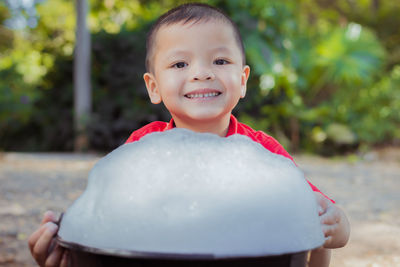 Portrait of smiling boy with soap sud in bucket sitting on land