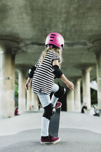 Rear view of girl performing stunt with skateboard at park