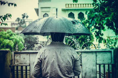 Rear view of man standing under umbrella during rainy season