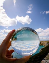 Midsection of person holding crystal ball against sky