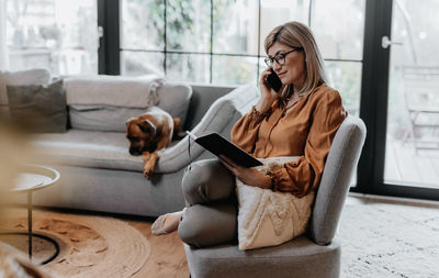 Businesswoman talking on phone while reading book at home