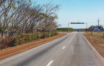 Empty road by trees against sky in city