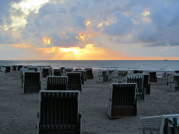 Wooden chairs on beach against sky during sunset